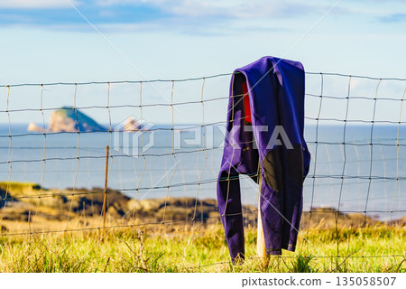 Diving suis drying on fence with sea view Diving suis drying on fence with sea view 135058507