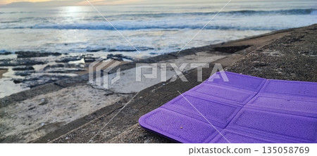 A brightly colored yoga or fitness mat resting on concrete steps by the ocean shore. The concept of mindfulness, outdoor exercise, healthy living, meditation and balance, stress relief, and self-care 135058769
