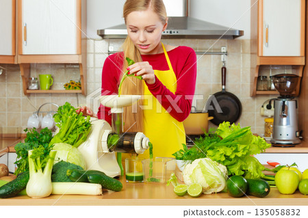 Woman in kitchen making vegetable smoothie juice 135058832