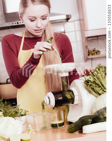 Woman in kitchen making vegetable smoothie juice 135058833