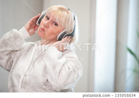 Elderly woman enjoys music in cozy indoor space while wearing stylish headphones 135058834