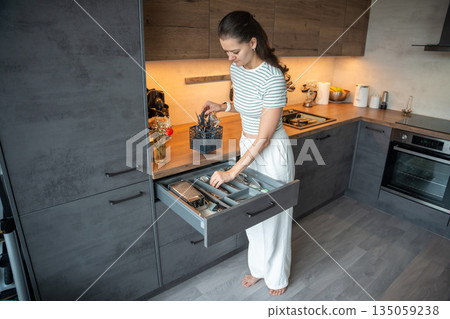 Woman organizing cutlery inside kitchen drawer at home. Everyday home organization process and domestic routine in real life interior Woman organizing cutlery inside kitchen drawer at home. Everyday home organization process and domestic routine in real life interior 135059238