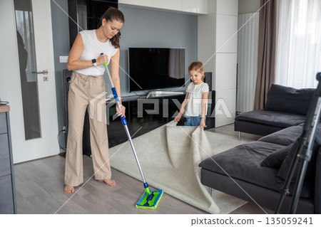 Mother and daughter cleaning floor with mop in living room at home. Everyday household chore and family routine in real life interior Mother and daughter cleaning floor with mop in living room at home. Everyday household chore and family routine in real life interior 135059241