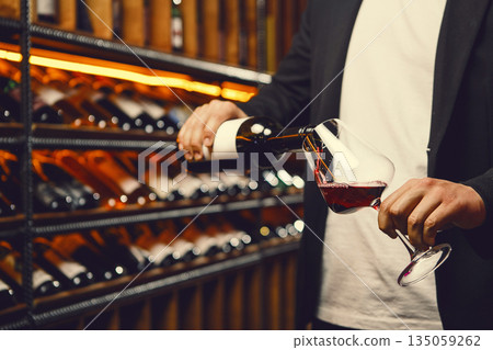 Faceless Man Pouring Red Wine into Glass in Cellar 135059262