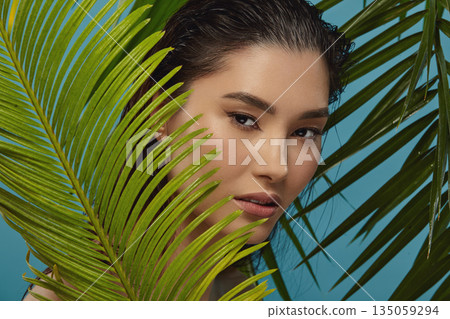 Oriental appearance girl surrounded by tropical plants leaves. Oriental appearance girl surrounded by tropical plants leaves. 135059294