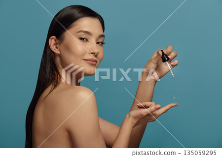 Asian woman keeps cap of cosmetic vial, looks to camera. 135059295