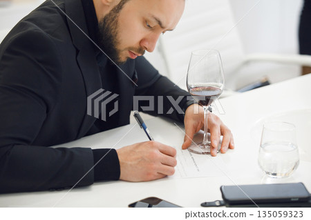Focused Sommelier in Black Attire Analyzing Wine Color ad Taking Notes at Professional Tasting Course Focused Sommelier in Black Attire Analyzing Wine Color ad Taking Notes at Professional Tasting Course 135059323