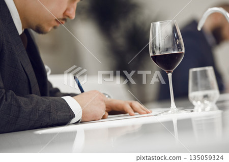 ProfessionalFaceless Sommelier Evaluating Red Wine by Tasting it and Making Notes to Wine Card of Participant. Wine study school, winemaking lecture. ProfessionalFaceless Sommelier Evaluating Red Wine by Tasting it and Making Notes to Wine Card of Participant. Wine study school, winemaking lecture. 135059324