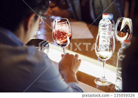 Sommelier Tasting Glass of Red Wine, Swirling it Sitting at Table Sommelier Tasting Glass of Red Wine, Swirling it Sitting at Table 135059326