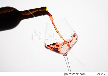 Pink wine pouring into tilted wineglass from bottle. Pink wine pouring into tilted wineglass from bottle. 135059347