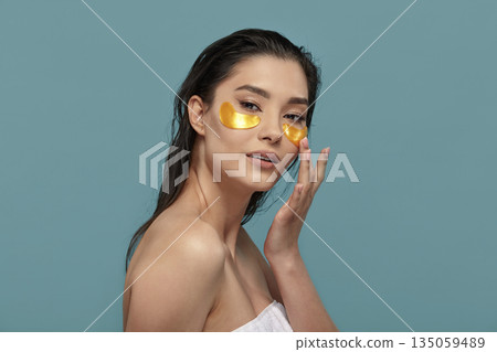 Well Groomed Woman with a Clean and Healthy Skin Applying Under Eyes Mask with Patches Standing on Blue Isolated Well Groomed Woman with a Clean and Healthy Skin Applying Under Eyes Mask with Patches Standing on Blue Isolated 135059489