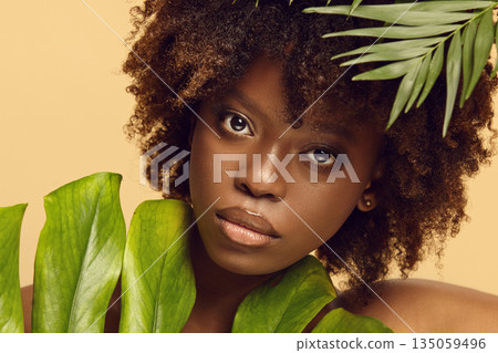 Portrait of black woman decorating her face with tropical leaves. Portrait of black woman decorating her face with tropical leaves. 135059496