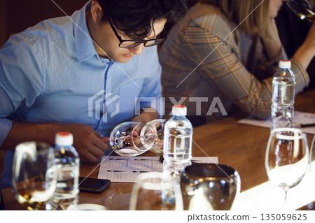 Man Analyzing White Wine at Table Participating in Sommelier Tasting Man Analyzing White Wine at Table Participating in Sommelier Tasting 135059625