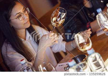 Woman Examining Two Wine Glasses at Table Being in Sommelier Tasting Woman Examining Two Wine Glasses at Table Being in Sommelier Tasting 135059626
