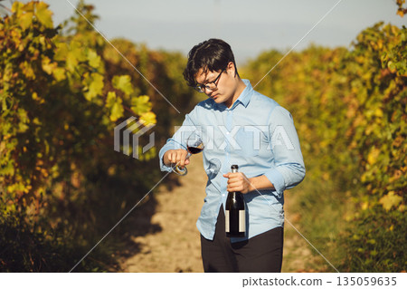 Male Sommelier Holding Glass of Red Wine Standing in Vineyard 135059635