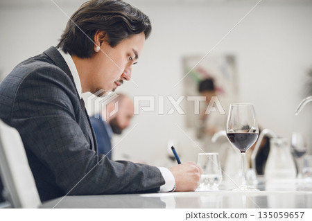 Focused Beginner Sommelier at Wine School is Training, Making Notes to Notebook. Sommelier Tasting Wine, Examination and Certification. 135059657