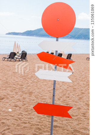 Wooden beach signpost with arrows on seaside promenade, copy space. Summer vacation, coastal leisure, and travel direction concept. Wooden beach signpost with arrows on seaside promenade, copy space. Summer vacation, coastal leisure, and travel direction concept. 135061869