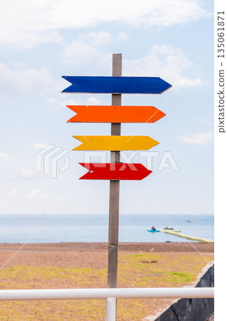 Wooden beach signpost with arrows on seaside promenade, copy space. Summer vacation, coastal leisure, and travel direction concept. 135061871