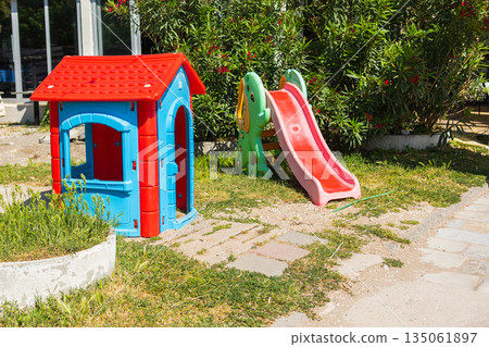 Colorful plastic playhouse and slide on green grass. Outdoor recreation, children play area, and summer leisure environment. 135061897