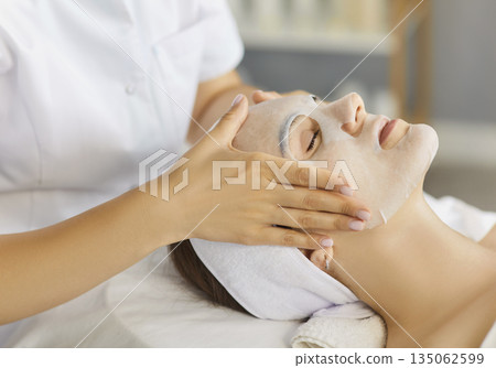 Closeup of esthetician massaging sheet mask in spa facial treatment session 135062599