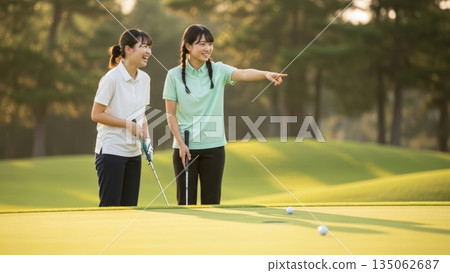兩個女孩一邊指著一邊讀著高爾夫球場果嶺上的線。 135062687
