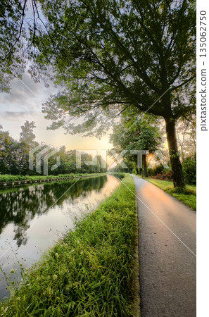 The Serene Riverbank at Sunset is Enhanced by Lush Greenery and Rich Colors around it 135062750