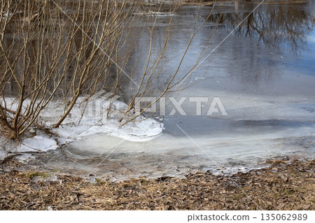 Ice crust on the bank of a frozen river in winter. River in water flows under frozen ice. 135062989