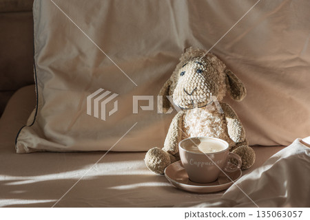 Knitted Sheep Toy with Cappuccino Cup on Cozy Bed in Sunlight 135063057