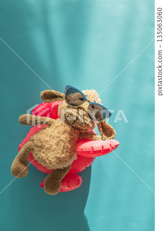 Knitted Plush Sheep in Sunglasses on Pink Flamingo Float Against Blue Water. Top view Knitted Plush Sheep in Sunglasses on Pink Flamingo Float Against Blue Water. Top view 135063060