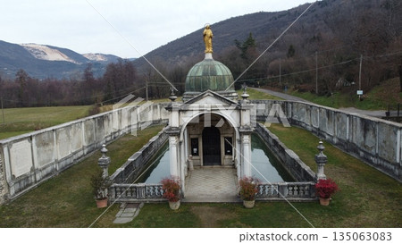Aerial view of the Sanctuary of Madonna di Valverde in Rezzato, Italy. Historic religious monument with a small lake and golden statue surrounded by mountains 135063083