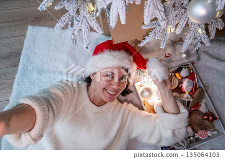 Woman in Santa Hat Enjoying Christmas Under Tree 135064103
