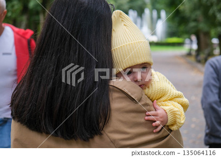 Mother Holding Baby in Yellow Outfit at Park 135064116