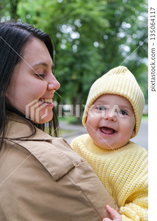 Mother Holding Baby in Yellow Outfit at Park 135064117