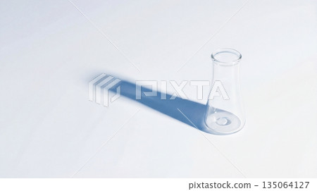 Clear glass Erlenmeyer flask standing on a white surface with a distinct blue shadow. Minimalist 135064127
