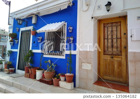 Vibrant blue house exterior with wooden door and potted plants in Alicante city Spain 135064182