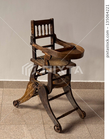 Antique wooden high baby chair with tray in empty room. Vintage furniture, craftsmanship and nostalgic atmosphere highlighting history and timeless design. 135064221