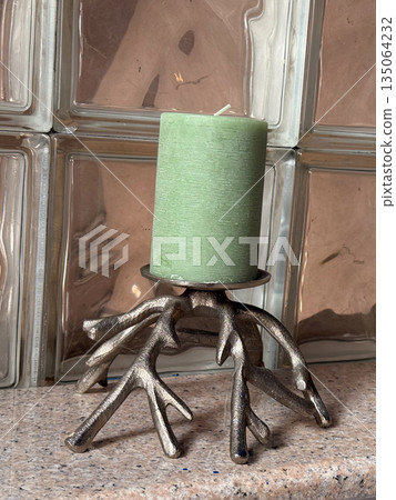 Green candle on metal stand with branch-shaped base. Artistic home decor, natural inspiration and elegant design blending organic and industrial elements. 135064232