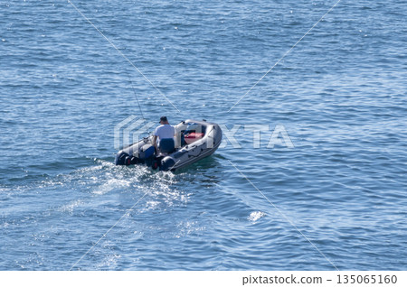 A fisherman in an inflatable boat on the sea. Calm water, clear sky, peaceful maritime scene 135065160