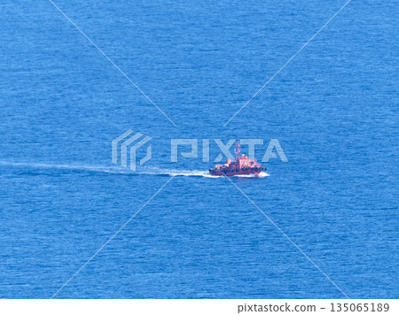 Red boat sailing in the distance on the open sea. Minimal marine landscape with water and horizon 135065189