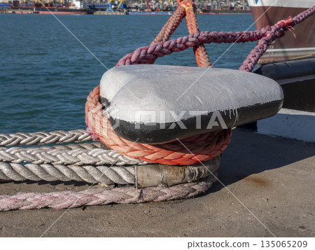 Mooring rope tied to a pier on the shore. Ship rope fastened to the dock in a mushroom shape Mooring rope tied to a pier on the shore. Ship rope fastened to the dock in a mushroom shape 135065209