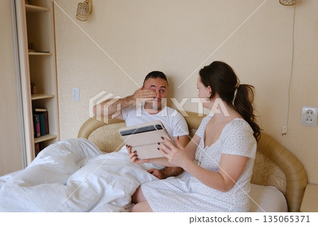 Happy couple enjoying a leisurely morning at home, sipping coffee and engaging with a digital tablet, sharing laughter and deepening their connection in a cozy kitchen setting Happy couple enjoying a leisurely morning at home, sipping coffee and engaging with a digital tablet, sharing laughter and deepening their connection in a cozy kitchen setting 135065371