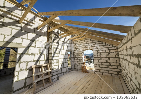 House interior under construction and renovation. Energy saving walls of hollow foam insulation blocks and bricks, ceiling beams and roof frame. House interior under construction and renovation. Energy saving walls of hollow foam insulation blocks and bricks, ceiling beams and roof frame. 135065632