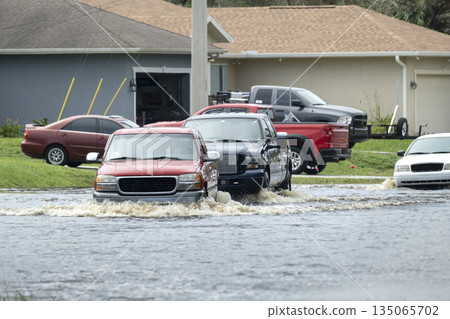Flooded road in Florida after heavy hurricane rainfall. Evacuating cars and surrounded with water houses in suburban residential area Flooded road in Florida after heavy hurricane rainfall. Evacuating cars and surrounded with water houses in suburban residential area 135065702