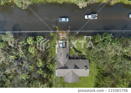Flooded american street with moving vehicles and surrounded with water houses in Florida residential area. Consequences of hurricane Ian natural disaster 135065706