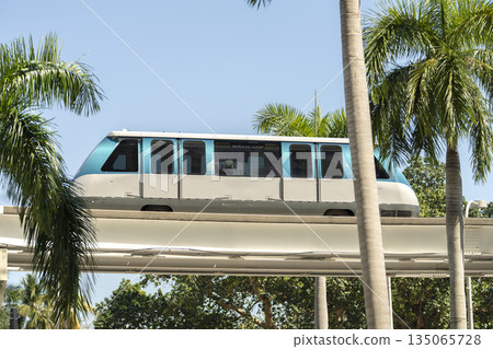Elevated train for public transportation in Miami city downtown district in Florida USA. Metrorail train car on high railroad over street traffic between skyscraper buildings in American urban area 135065728