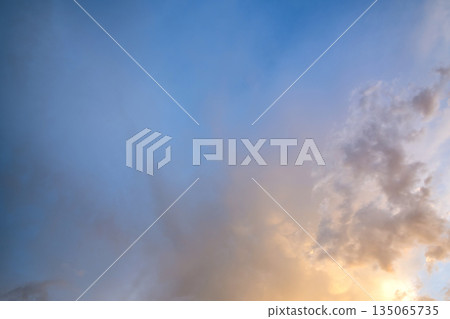 Dramatic sky at sunset with puffy clouds lit by orange setting sun. 135065735