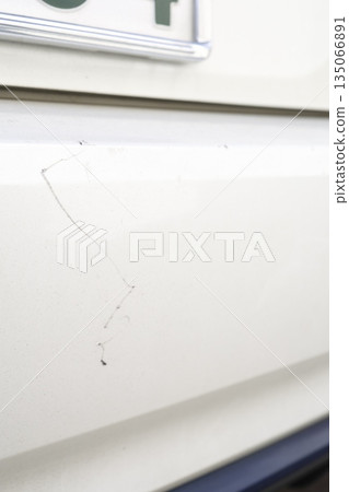 Close-up of a scratch on the rear bumper of a white car. Close-up of a scratch on the rear bumper of a white car. 135066891
