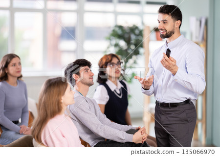 Male lecturer communicates with students, controls projector using remote control. Male lecturer communicates with students, controls projector using remote control. 135066970