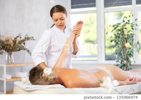 Professional young female massage therapist doing back massage to woman Professional young female massage therapist doing back massage to woman 135066974
