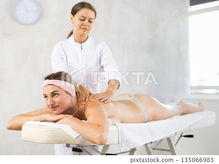 Girl enjoys and rests during back and shoulder massage procedure in beauty salon Girl enjoys and rests during back and shoulder massage procedure in beauty salon 135066983